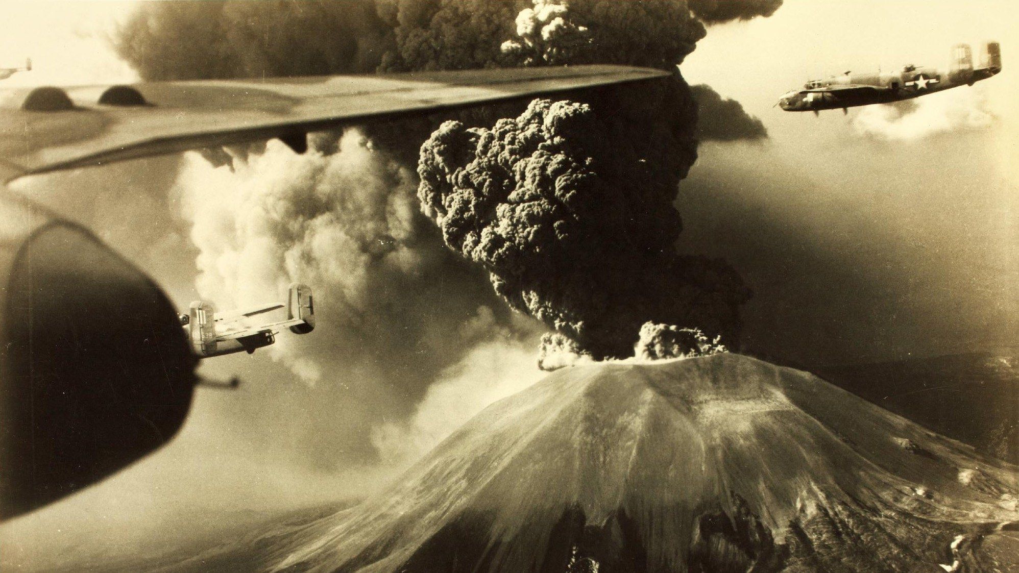 Foto aerea del marzo 1944: dal cratere del Vesuvio sale una colonna scura di cenere mentre alcuni bombardieri B-25 americani volano accanto